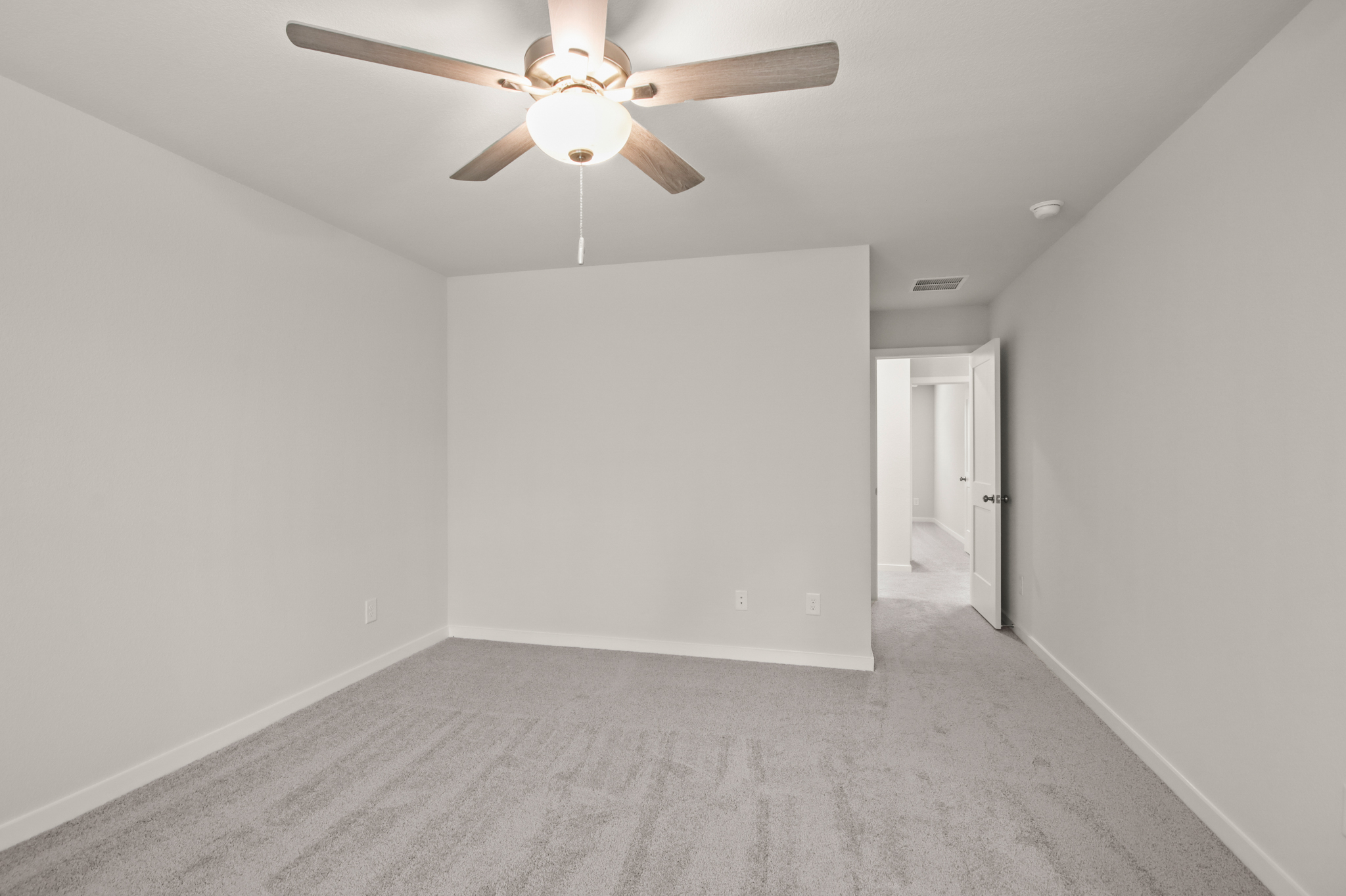 A room with a ceiling fan and white walls.
