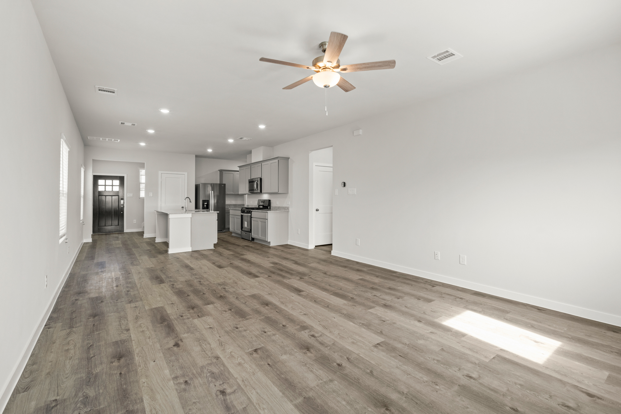 A large empty room with a ceiling fan and a wood floor.